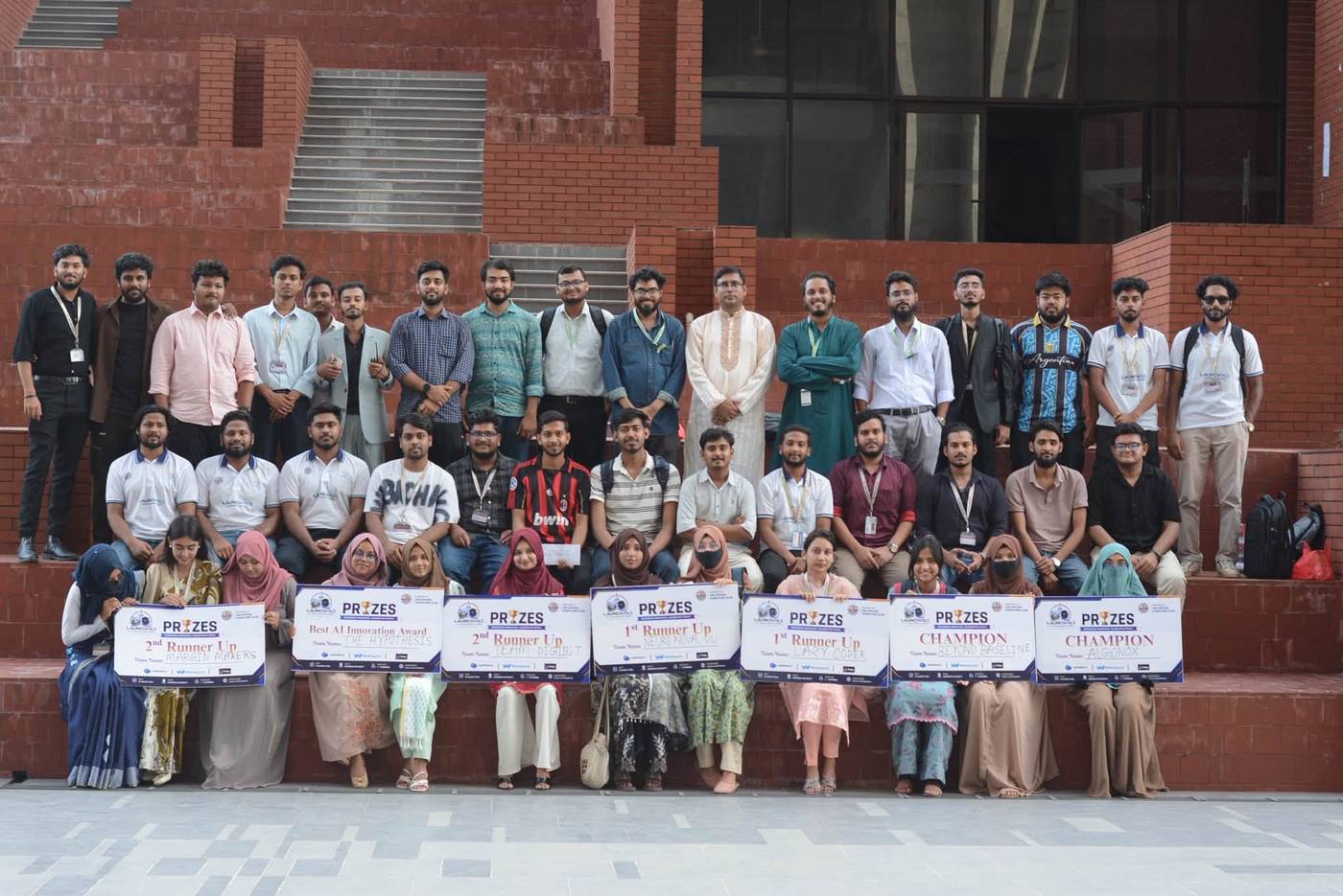 Students holding hackathon prize boards on the red brick steps of the campus