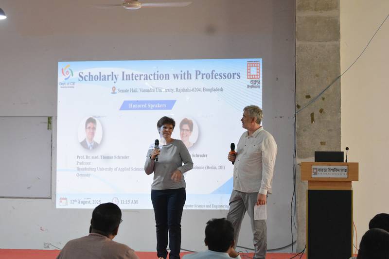 Two visiting professors speaking in front of a presentation slide