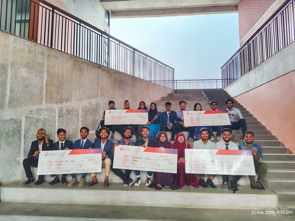 Teams holding large cheques on a campus staircase